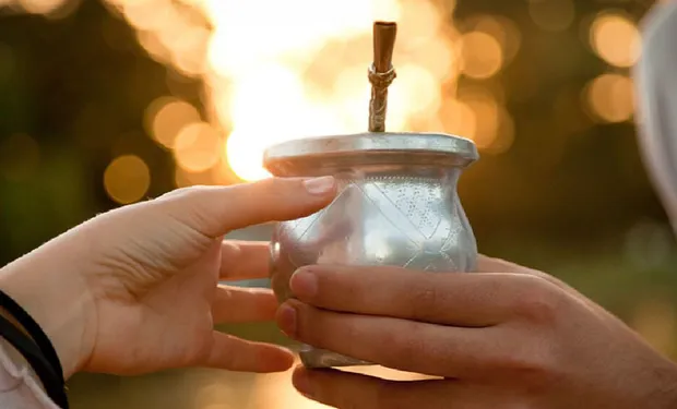 Hands sharing a traditional Argentine mate gourd with a metal straw at sunset — symbol of connection and South American culture. Hands sharing a traditional Argentine mate gourd with a metal straw at sunset — symbol of connection and South American culture.