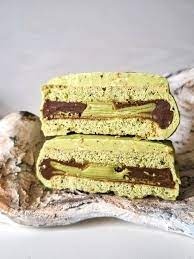 Argentine alfajor with pistachio filling and dulce de leche layer, sliced in half on a ceramic plate.