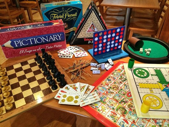 Juegos de mesa clásicos como Pictionary, Trivial Pursuit, ajedrez, Ludo, cartas y dominó sobre una mesa