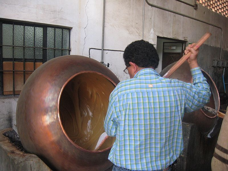 Traditional dulce de leche being stirred in large copper kettle during artisanal production.