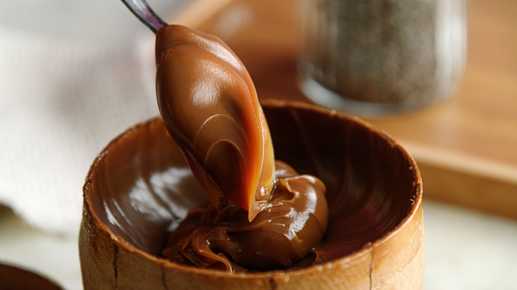 Close-up of creamy Argentinian dulce de leche on a spoon, served in a rustic wooden bowl.
