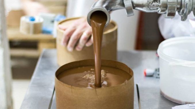 Producción de dulce de leche en fábrica, llenado de envases con maquinaria industrial.